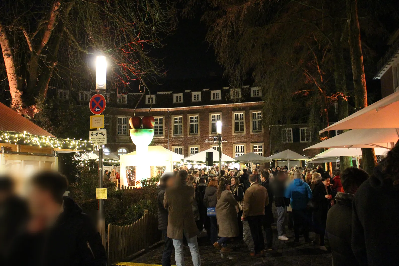 X-MS Christmas market on Harsewinkelplatz in Münster by Thomas Schütte's Kirschensäule sculpture, with stalls and visitors.